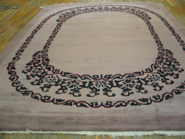 A muted taupe plush rug with a bold black and red floral scroll medallion on a wood floor.