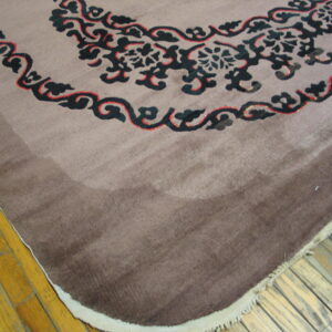 Mauve and brown shaded rug displaying dark blue and red scrolling patterns rests on yellow wood planks.