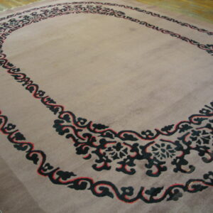 Mauve low-pile area rug with an intricate black and red scroll pattern border on wood flooring.