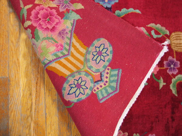 A burgundy floral rug corner folds over worn wood, revealing a pink backing with brightly woven pattern details.