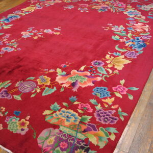 Crimson rug with a large, multi-colored floral and vine pattern displayed on rustic wood flooring.