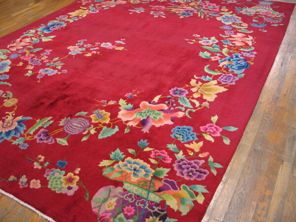 Crimson rug with a large, multi-colored floral and vine pattern displayed on rustic wood flooring.
