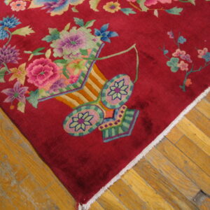 Close-up of a crimson rug featuring colorful floral bouquets and a decorative vase motif on wood planks.