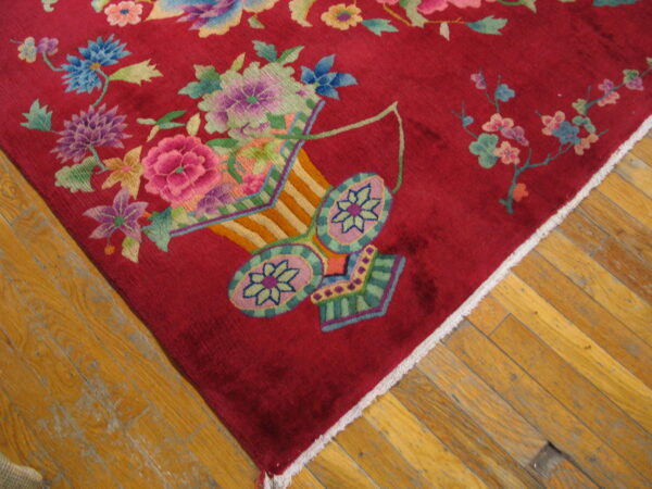Close-up of a crimson rug featuring colorful floral bouquets and a decorative vase motif on wood planks.