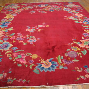 High-pile crimson rug displaying vibrant floral patterns around a solid center on light hardwood flooring.