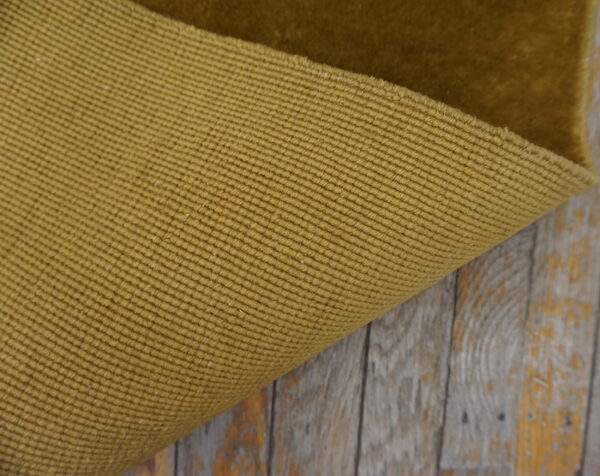 Close-up shows the tight, ribbed backing of a mustard rug on weathered wood.