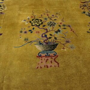 Textured golden rug with a detailed multicolored central motif of a potted flowering tree and scattered florals.