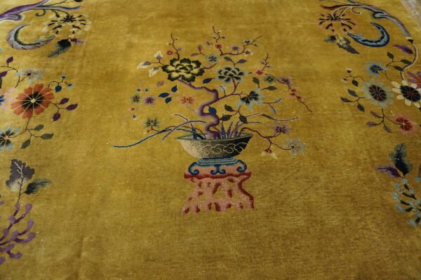 Textured golden rug with a detailed multicolored central motif of a potted flowering tree and scattered florals.