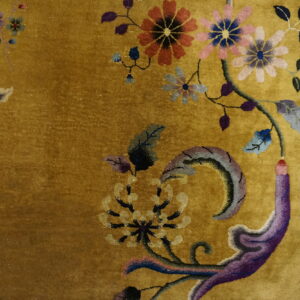 Close-up of a golden rug with colorful floral motifs next to worn wood plank flooring.