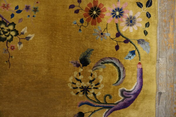 Close-up of a golden rug with colorful floral motifs next to worn wood plank flooring.