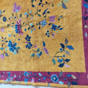 Close-up of a mustard gold rug with intricate blue, purple, and green floral vines and a thick magenta border.