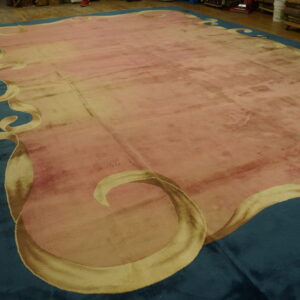 A large plush pink rug with a teal ribbon border is displayed on wide plank wood flooring.