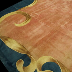 Mottled pink rug field with gold scroll designs bordering a section of dark teal blue.