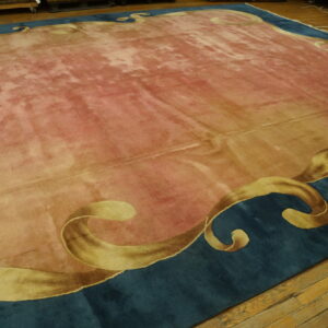 Rose-colored rug with distressed shading and a teal border featuring large scrolling gold motifs on wood flooring.