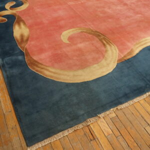 A plush pink and blue rug with a flowing gold ribbon pattern rests on worn wood plank flooring.