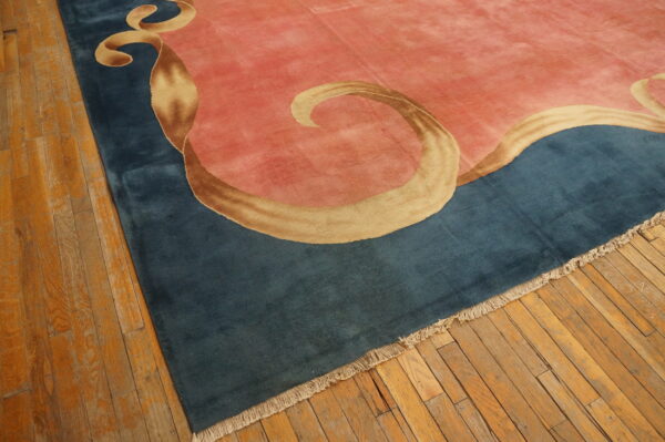 A plush pink and blue rug with a flowing gold ribbon pattern rests on worn wood plank flooring.