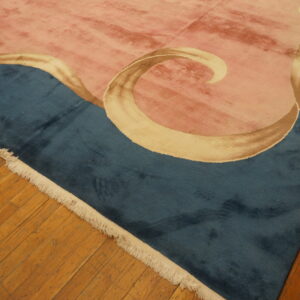 Dusty rose and deep teal rug with flowing tan ribbons lies on natural plank hardwood flooring.