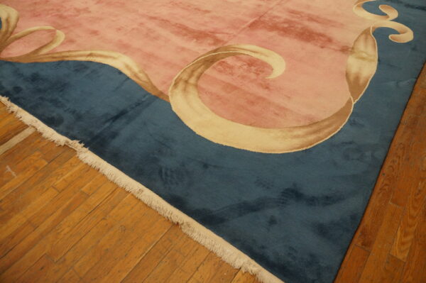 Dusty rose and deep teal rug with flowing tan ribbons lies on natural plank hardwood flooring.