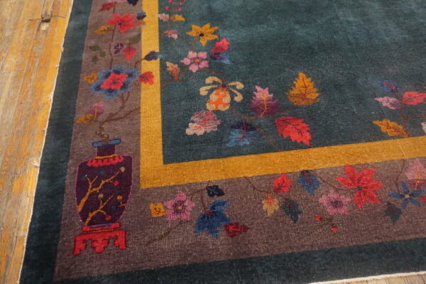 Teal rug with a colorful floral and vase pattern, brown border, and gold stripe on distressed wood floor.