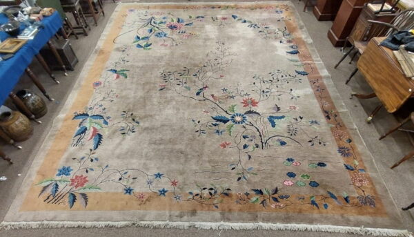 Muted beige rug featuring sprawling blue and pink blossoming tree branches and birds within a wide tan border.