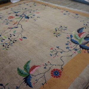Low-pile beige rug displaying a detailed colorful floral and bird pattern with a wide gold border.