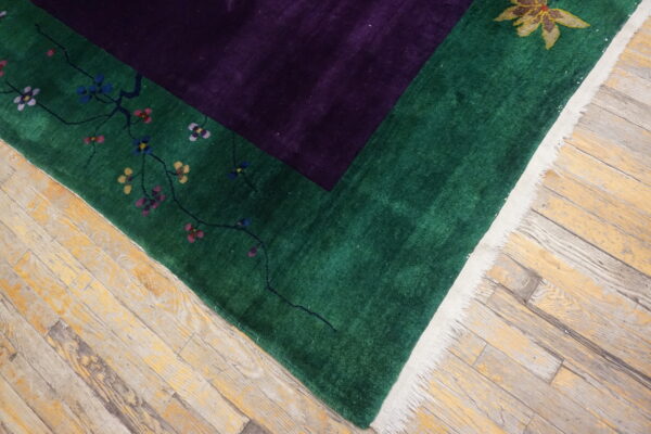 Deep purple field and green border rug featuring colorful florals, visible on worn wood plank flooring.