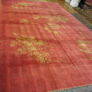 A large pinkish-red, high-sheen rug with gold floral patterns displayed on wood flooring.