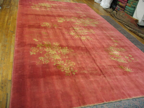 A large pinkish-red, high-sheen rug with gold floral patterns displayed on wood flooring.