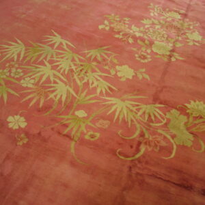 Pink distressed rug featuring light green floral clusters and large bamboo-like leaves.