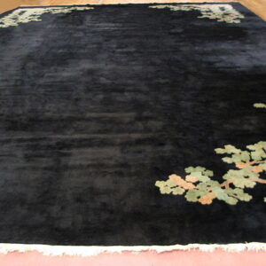 Dark, lustrous rug featuring large-scale green and tan branch motifs on the corners, displayed with white fringe.