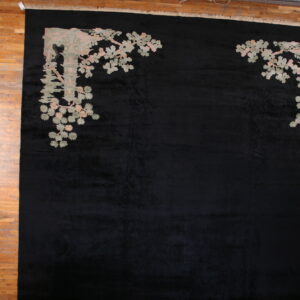 Large black rug features pale pink and sage corner motifs of architecture and foliage on wood planks.