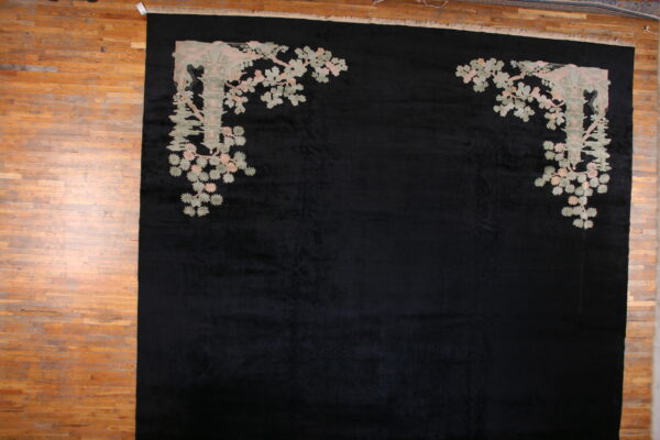 Large black rug features pale pink and sage corner motifs of architecture and foliage on wood planks.