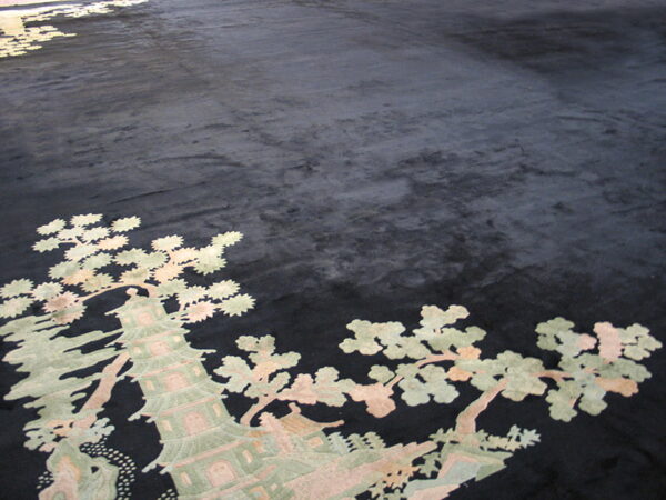 Black plush rug with a detailed asian-style pattern of a pagoda and trees in muted green and pink.