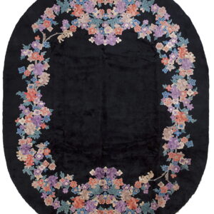 Plush black oval area rug bordered by an intricate wreath of coral, lavender, and blue flowers.