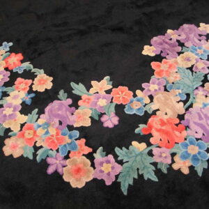 A high-pile black rug features a curving border of dense floral motifs in coral, purple, blue, and sage green.