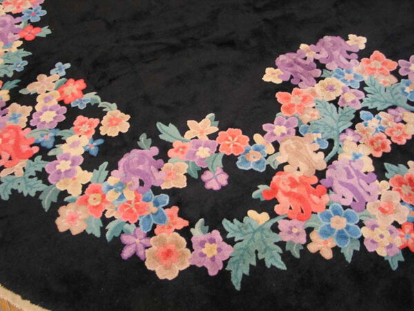 A high-pile black rug features a curving border of dense floral motifs in coral, purple, blue, and sage green.