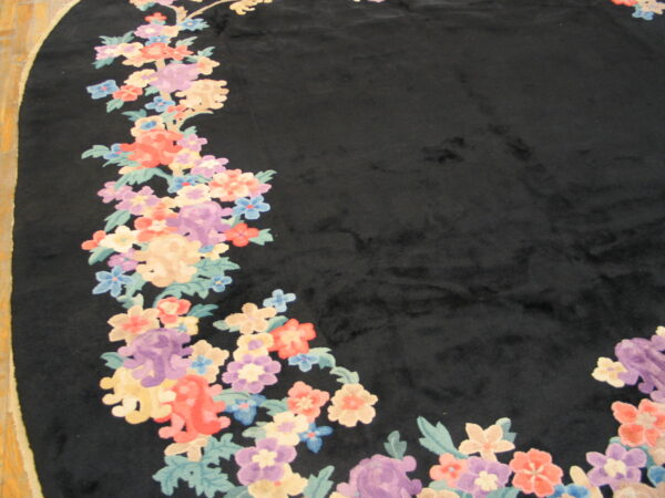 Black high-pile rug with colorful floral garland border in pastel hues rests on wood flooring.
