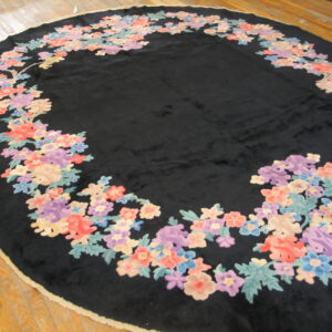 High-pile oval black rug framed by a border of colorful floral elements on wood planks.