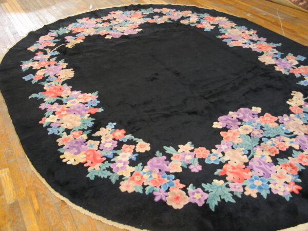 High-pile oval black rug framed by a border of colorful floral elements on wood planks.