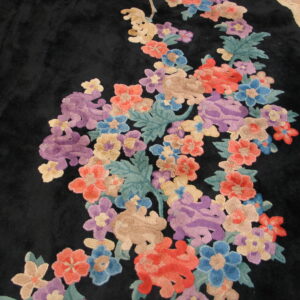 Plush black rug with vivid sculpted floral motifs in shades of purple, red, and blue on wood flooring.