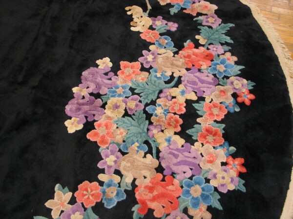 Plush black rug with vivid sculpted floral motifs in shades of purple, red, and blue on wood flooring.