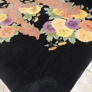 Black rug with bright yellow, orange, and purple floral patterns resting on light distressed wooden floors.