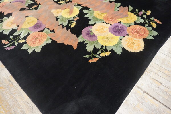 Black rug with bright yellow, orange, and purple floral patterns resting on light distressed wooden floors.