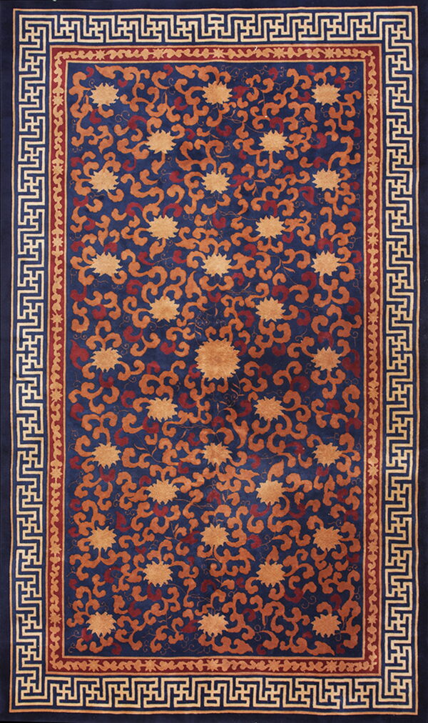 Navy blue rug displays an orange and red repeating floral pattern with a bold geometric key-fret border.