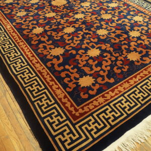 Navy blue, gold, and rust patterned rug with geometric borders rests on rustic light wood floors.