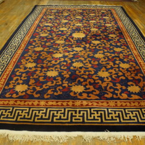 A navy blue rug with gold and rust floral motifs features a distinctive key pattern border on a wood floor.