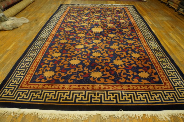 A navy blue rug with gold and rust floral motifs features a distinctive key pattern border on a wood floor.