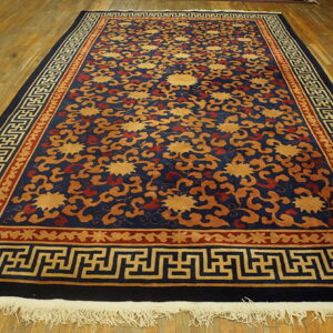 Navy blue rug with gold floral patterns and complex geometric borders on a wood plank floor.
