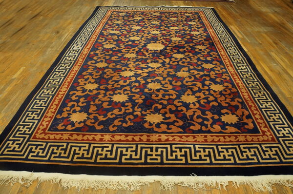 Navy blue rug with gold floral patterns and complex geometric borders on a wood plank floor.