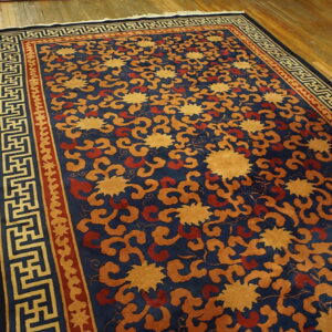 A navy rug with mustard yellow and rust floral patterns features a geometric border on wood floorboards.